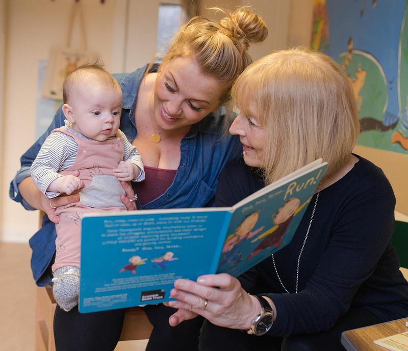Two women reading a picture book with a baby
